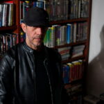 Uomo con libreria alle spalle piena di musicassette